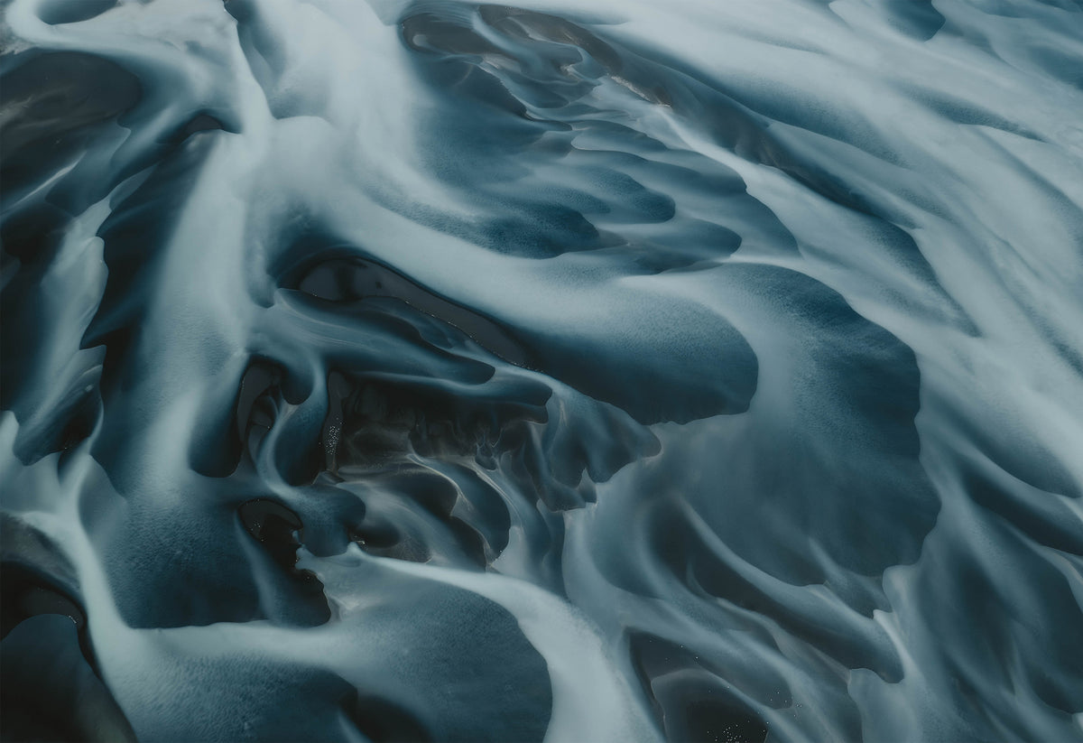Aerial view of an Icelandic river flowing toward the sea, with blue and white patterns resembling veins – fine art travel photograph by Sam Morris.