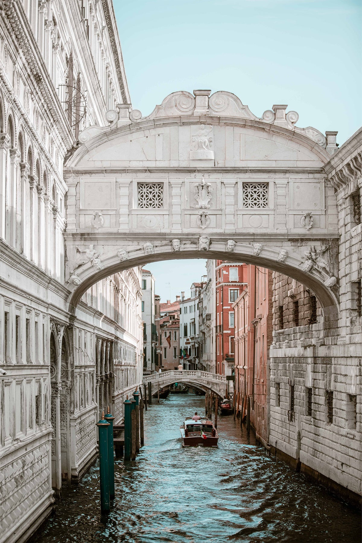 The Bridge of Sighs in Venice with the canal shimmering blue and a boat driving under - a fine art photography print by Charles Johnstone.