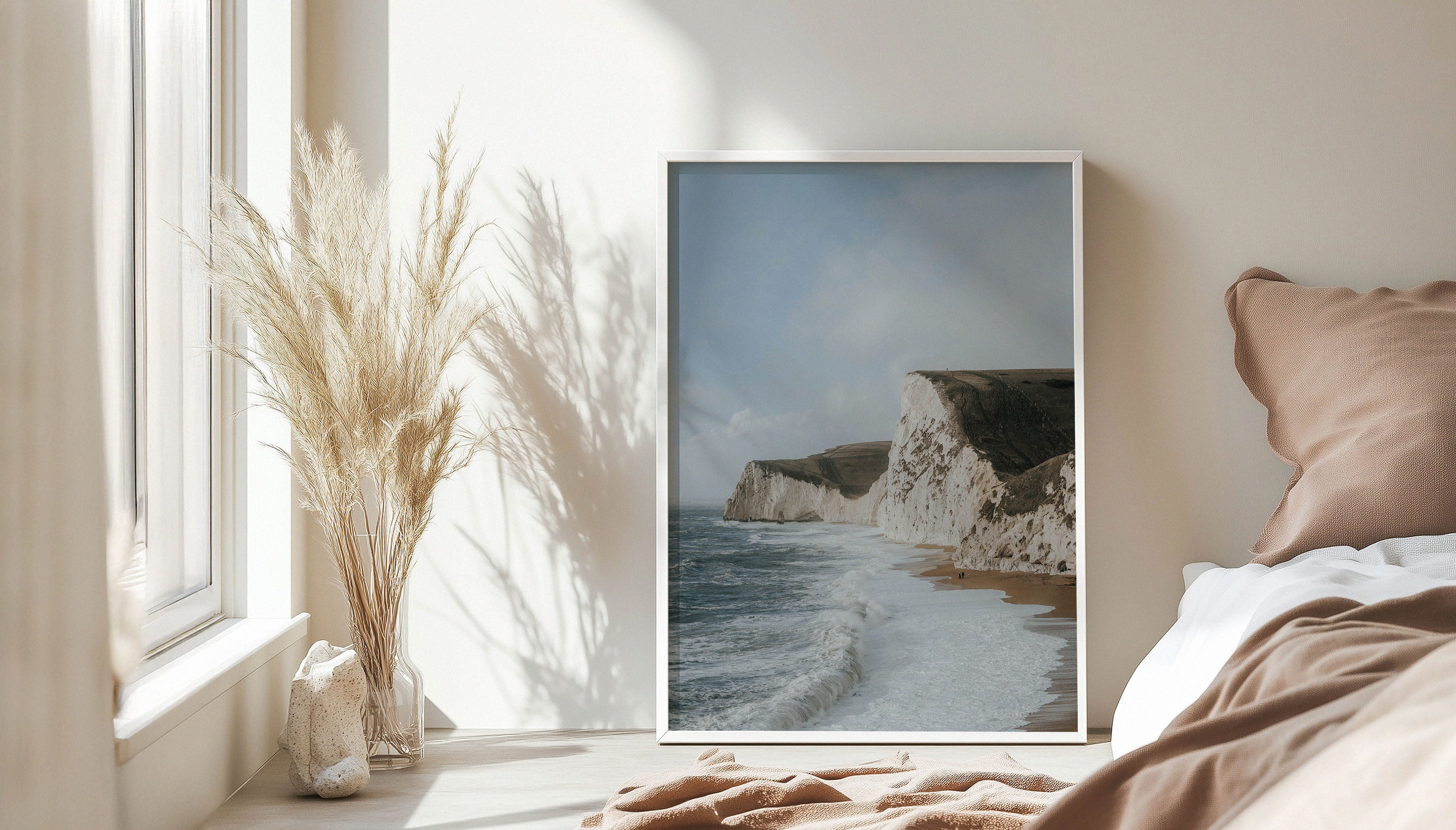 Sam Morris' fine art travel photograph, capturing dramatic sea cliffs and the wild coastline along England’s Jurassic Coast under blue skies, shown in a white frame leaning against a bedroom wall.
